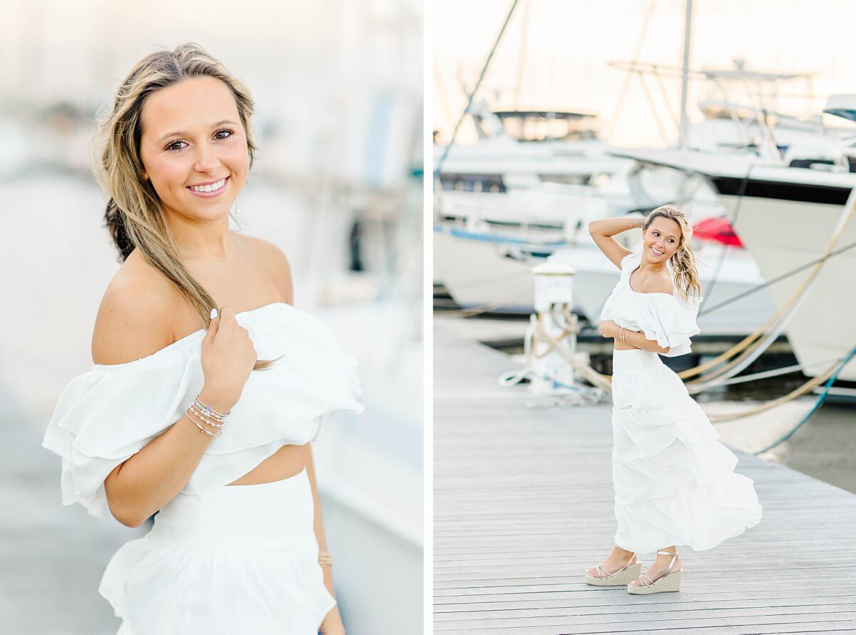 High school senior in a white two-piece outfit posing on the dock at New Bern marina with boats in the background and wind in her hair